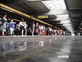 Multiple people wait at the long platforms of a station.