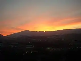 Sunset lights up the sky, silhouetting a long, notched ridge with a prominent peak toward its left-hand (southern) end.