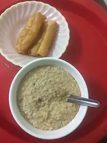 Thick, brown, medium textured porridge in bowl next to plate of fried tofu.