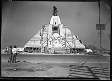 Black-and-white picture of the pyramid as seen from the east side. It is surrounded by several workers and wooden beams.