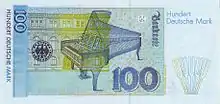 Banknote in light blue with yellowish green and beige, focused on an open grand piano, with a building in the left background