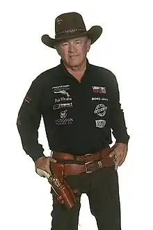 Man wearing a cowboy hat and pistol in its holster, with both hands on hips