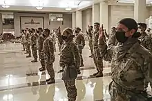 Multiple people in fatigues raising their right hands lined in a grid. They are all wearing masks.