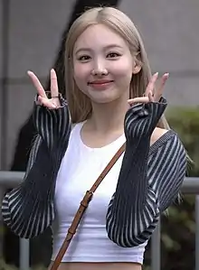 Nayeon smiling and giving two peace signs while looking at the camera