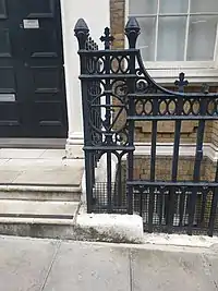 Metal railings around the same factory building, with a design showing a V, J and F