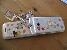 A Japanese flip phone typical of the 2000's with phone charms.  These phones and charms were symbolic of youth culture in the early Heisei era, and remained prevalent in Japan long after the advent of the smartphone made flip phones obsolete elsewhere.