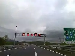 Variable traffic signs placed on a gantry spanning three motorway traffic lanes, indicating slippery pavement and reduced speed limit