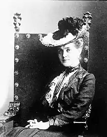 A white woman with dark hair, wearing a dark gown with long sleeves and sequins.