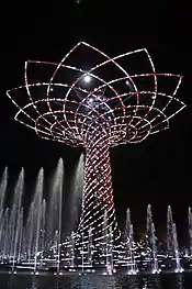 Large tree made of lights at night, surrounded by fountains