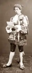 Clean-shaven white man in 18th century costume, reading a letter and looking shocked