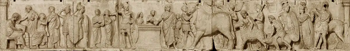 Relief depicts a long continuous scene that may be divided into three main groupings from left. The first is a group of four men wearing togas. Two are seated, and one is writing in a tablet. Two tall military guards divide this group from the central scene of sacrifice. Two musicians, markedly shorter than the soldiers, play a lyre and a horn. An unadorned altar, waist-high, stands in the center. To the viewer's left is the tallest figure in the composition, a military officer wearing a high plumed helmet and holding a long slender spear. standing by an altar. On the other side of the altar a priest, his head ritually covered, extends a libation bowl. A boy attendant pours from a pitcher into the bowl, and to that boy's right is a smaller boy looking on and lifting his right hand to the top of his head, a gesture that appears quizzical to modern viewers but may have some other significance in its Roman context. The priest is accompanied by a third boy close to his left side who stands ready with a towel. The right side of the relief is devoted to the procession of the three animal victims for the suovetaurilia, each led by a young male attendant, barechested but wearing a short kilt-like garment, with a wreath on his head. The first leads an enormous bull with a tasseled rope dangling from below its left horn. A fourth male attendant in the same attire follows closely on the bull's hindquarter, waving a palm branch in each hand. The attendant bringing the ram is followed by another veiled figure carrying a pole from which a banner unfurls. The attendant herding the pig is followed by another soldier bearing a long shield and looking back at another whose shield rests on the ground, covering most of his body. The last figure is a cavalryman, back turned to the viewer, next to his horse.