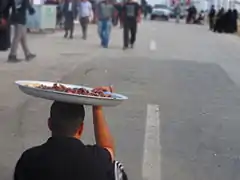 A man holding a plate full of dates on his head for passing Arba'een pilgrims