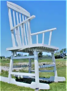 A large wooden rocking chair painted white against a blue sky and grass.