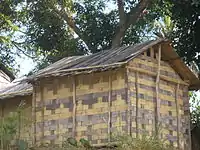 Small, rectangular one-room house with walls and roof made of flattened bamboo