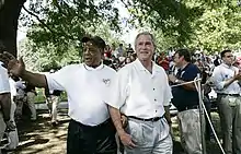 Photograph of Mays and President George W. Bush wearing white polo shirts walking past a crowd of people; both are smiling and Mays is waving