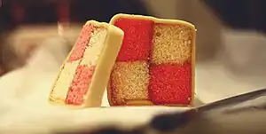 Homemade Battenberg cake covered in marzipan and, when cut in cross section, displaying a distinctive two-by-two check pattern alternately coloured pink and yellow