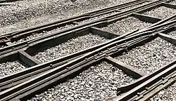 Three rails cross the picture from left to right supported on thick timbers; occasional smaller timbers cross between these and stone chippings fill the space between them.