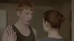 A woman with painted nails touches hands with a robotic-looking man wearing a green vest.