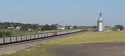 Cluster of houses seen over railroad tracks occupied by train; metal grain elevator