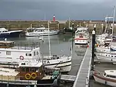 small boats lined up in harbour. Crane in the background & metal walkway in the foreground.