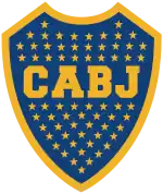 A Blue shield with a golden border. Inside the shield, 67 stars inside the shield with the golden letters "CABJ" (meaning "Club Atlético Boca Juniors") printed around the center, separating the stars