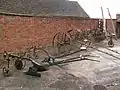Display of farm machinery in the yard: single furrow plough, potato plough, and rakes.