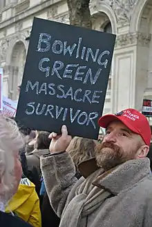 Man holding sign that reads "Bowling Green Massacre Survivor"