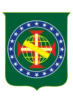 Coat of arms consisting of a shield with a green field with a golden armillary sphere superimposed on the red and white Cross of the Order of Christ, surrounded by a blue band with 20 silver stars; the bearers are two arms of a wreath, with a coffee branch on the left and a flowering tobacco branch on the right; and above the shield is an arched golden and jeweled crown.