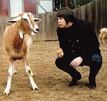 Wilson kneeling down face-to-face with a goat