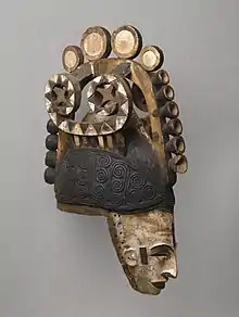 Igbo maiden spirit helmet mask (Agbogho Mmwo); early 20th century; 50.2 x 14.6 x 30.5&nbsp;cm (19.mw-parser-output .frac{white-space:nowrap}.mw-parser-output .frac .num,.mw-parser-output .frac .den{font-size:80%;line-height:0;vertical-align:super}.mw-parser-output .frac .den{vertical-align:sub}.mw-parser-output .sr-only{border:0;clip:rect(0,0,0,0);clip-path:polygon(0px 0px,0px 0px,0px 0px);height:1px;margin:-1px;overflow:hidden;padding:0;position:absolute;width:1px}3⁄4 x 5.mw-parser-output .frac{white-space:nowrap}.mw-parser-output .frac .num,.mw-parser-output .frac .den{font-size:80%;line-height:0;vertical-align:super}.mw-parser-output .frac .den{vertical-align:sub}.mw-parser-output .sr-only{border:0;clip:rect(0,0,0,0);clip-path:polygon(0px 0px,0px 0px,0px 0px);height:1px;margin:-1px;overflow:hidden;padding:0;position:absolute;width:1px}3⁄4 x 12 in.); Brooklyn Museum. This helmet mask has long narrow face, painted white; narrow protruding sharp nose; slit eyes; open mouth showing teeth; small ears