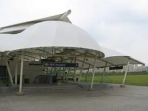 Buangkok station entrance with a white canopy. The entrance faces an open field.
