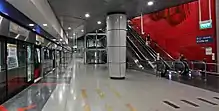 A train arrives at the CCL platform (on the left). The artwork of glass fins is on the red wall on the right, above the escalators.