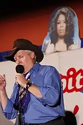 Man onstage in a Stetson hat in front of a picture of Oprah Winfrey
