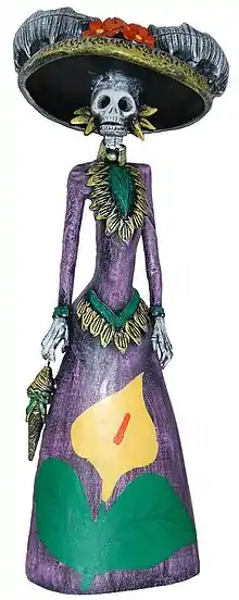 A photograph of a sculpture of a skeletal figure in a brightly-colored, feminine outfit and hat.