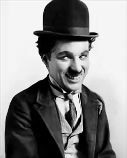 A smiling man with a small moustache wearing a bowler hat and a tight-fitting necktie and coat