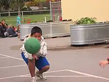 A boy crouching with a green utility ball speeding toward him