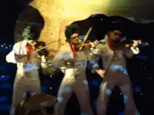 Three men dressed as Elvis Presley impersonators play the violin