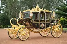 A very ornate coach, black with gold trim, a coat of arms on the door