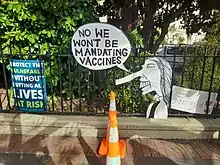Anti-government sign attached to a railing states, "No, we won't be mandating vaccines", with a caricature of Ardern sporting a Pinnochio nose.