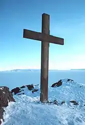 Flat-topped hill with snow on lower slopes and sea in the foreground, and a solitary bird in flight