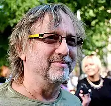 Close-up of middle-aged white man with facial stubble, wearing glasses, looking to the left of the camera
