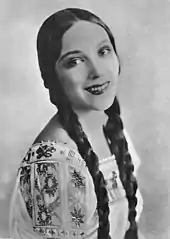 Del Río smiling, wearing a dress, and with her hair in braids looking directly to a camera
