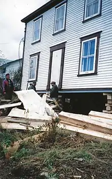 Three men are shown in the process of jacking up the foundation of a two-storey house