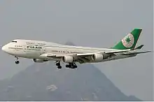Aircraft in flight. Side view of quad-engine jet with extended landing gear and flaps.