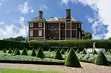 A photograph of the east side of the house taken from the Cherry Garden, which is notable for its formally-landscaped pattern including conical firs