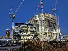 Shells of two buildings under construction by cranes. One is composed of rectangular blocks, the other is more angular