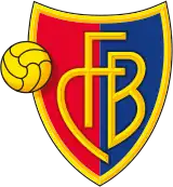 FC Basel crest of a shield, the left half red and the right half blue. The shield is outlined with gold and in the centre in gold letters it reads "FCB". On the left side of the logo is a gold football.