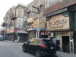 A street with parked cars and several shops with appartements above them.