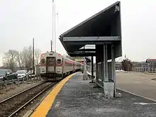 A passenger train at a low-level railway platform with an angular shelter