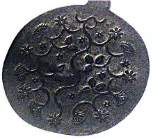 Round metal plate decorated with raised pattern of flowers, vines, and leaves